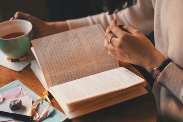 a woman sits at a table reading a journal with a cup of tea. Introverts tend to be deep thinkers, aiding in content creation.